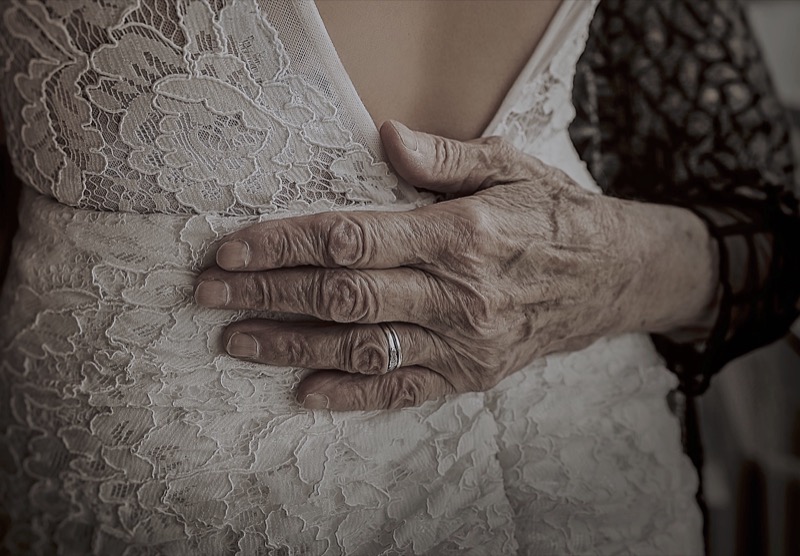 Elderly hand on bride lace dress back, detail wedding photography