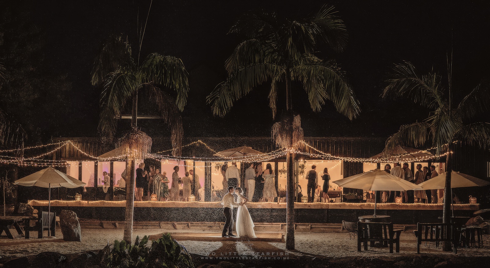 Bride and groom kissing in the rain with fairy lights